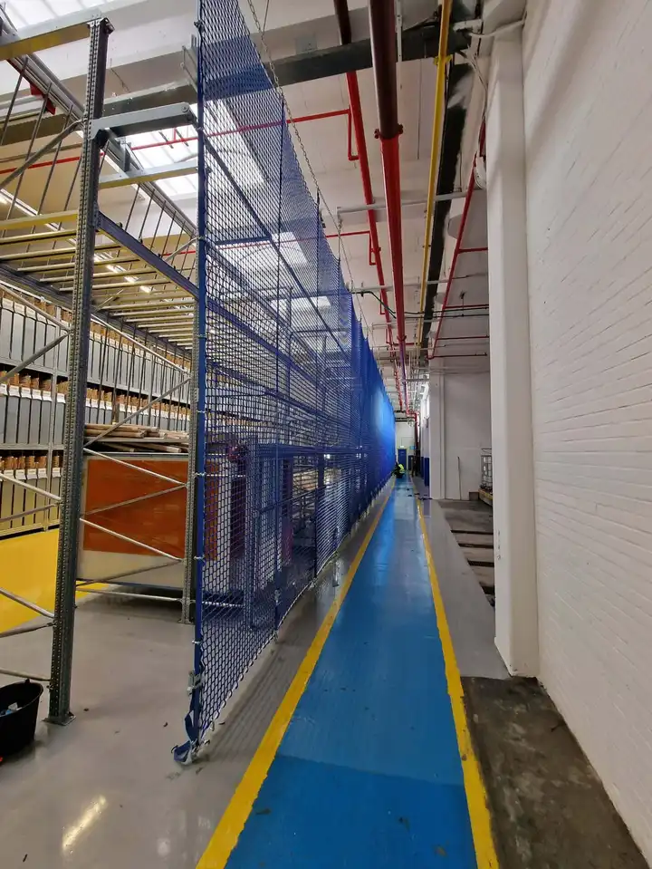 Blauw stellingnet langs een gangpad tussen stellingen